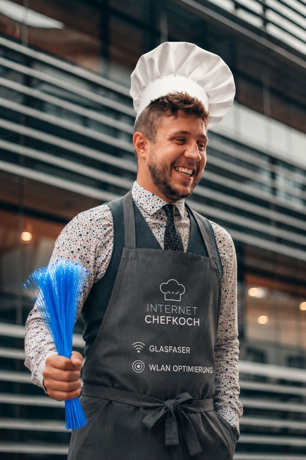 Marcel im Chefkoch-Look lacht und hält blaue Glasfaser-Fäden in der Hand